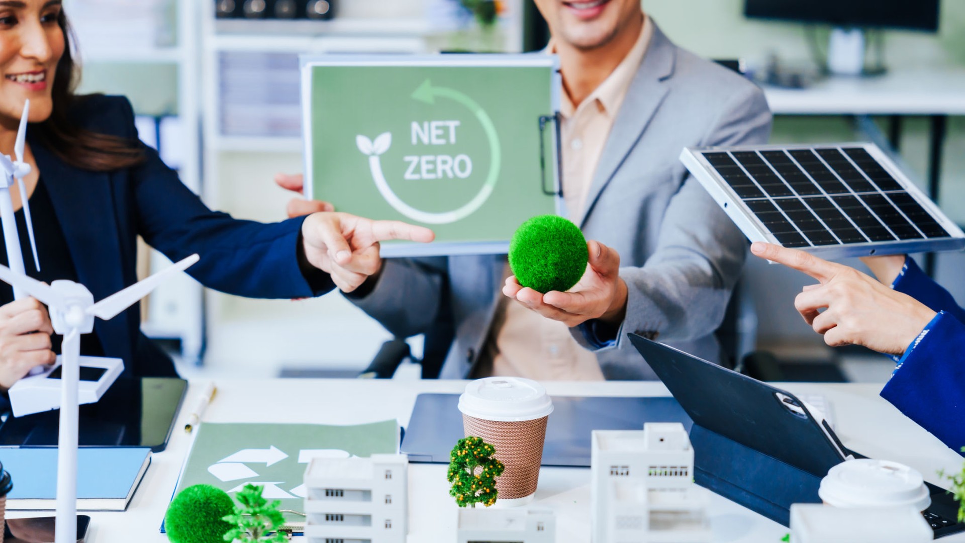 Trio of businesspeople, including a middle-aged Asian man and woman, strategize at their desk, prioritizing sustainability renewable energy adoption, waste reduction, and eco-friendly practices.